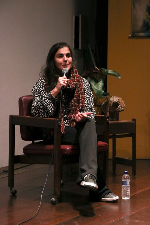 Lâne no palco, se encontra sentada em uma cadeira e discursa com microfone