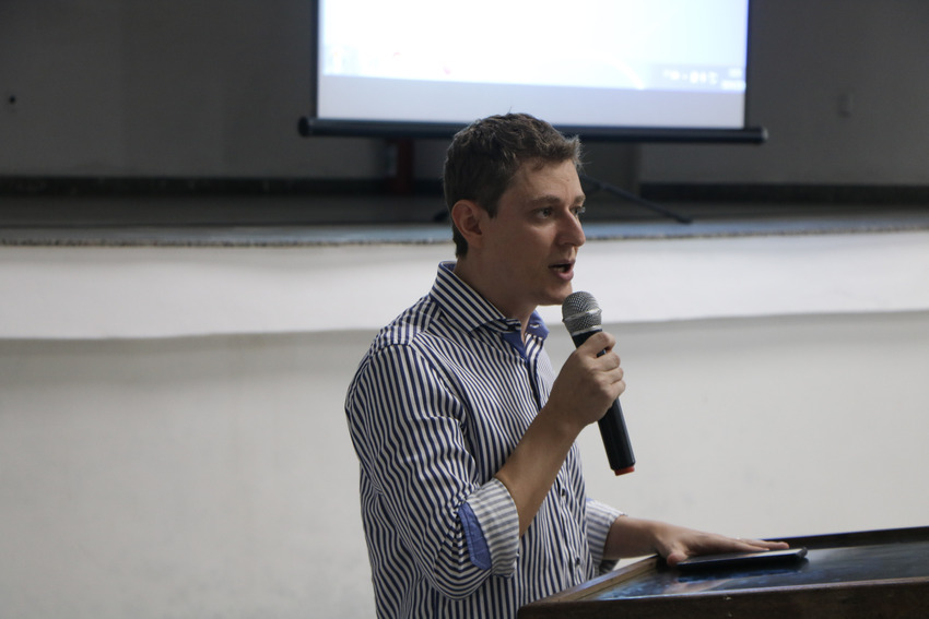 Harrisson fala ao microfone, está vestido com cores claras. O diretor do Icsa da boas-vindas aos estudantes dos cursos.