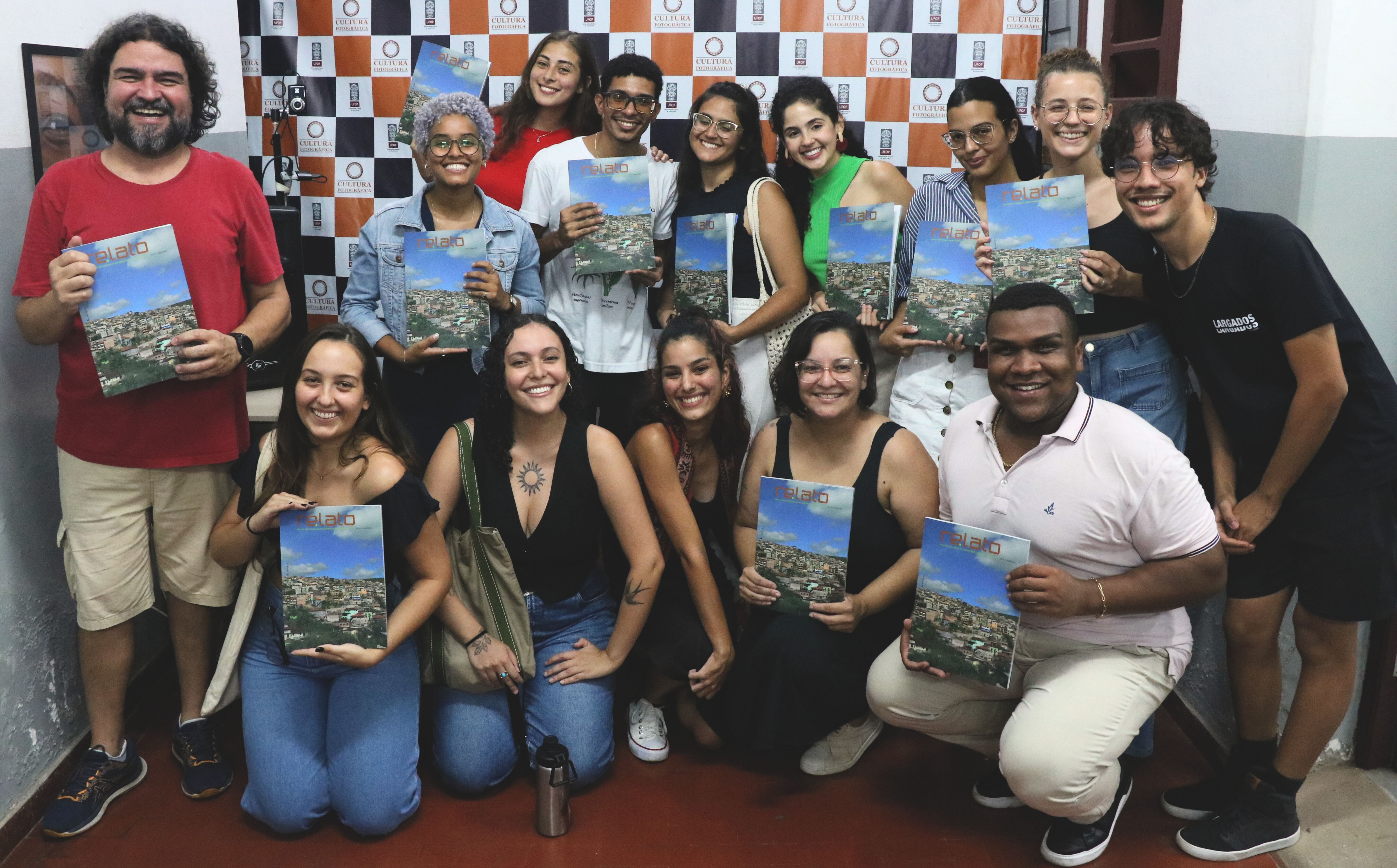 Imagem de alunos e professores sorrindo segurando uma revista azul 