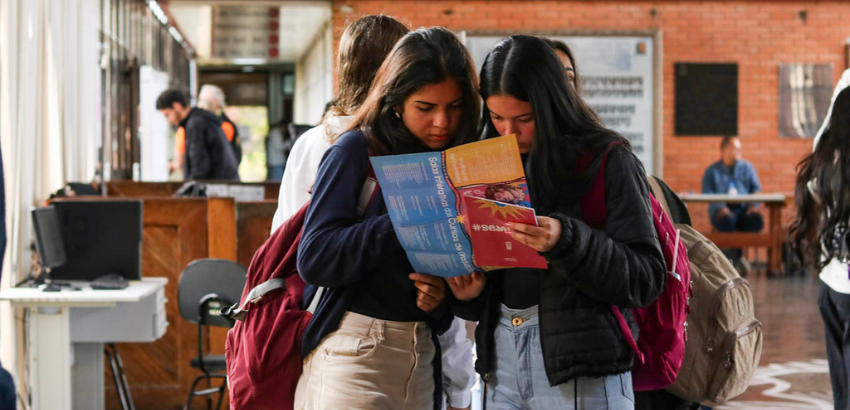 No hall da Escola de Minas, duas jovens olham para o folder da Mostra de Profissões