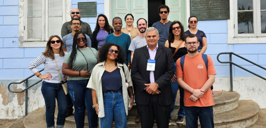 O ChatGPT disse:  Grupo de cerca de 14 pessoas posa em frente a um prédio histórico de fachada azul e janelas brancas. Entre os participantes, homens e mulheres sorridentes, alguns com crachás, representando os visitantes do VIII ENARQUIFES na UFOP.