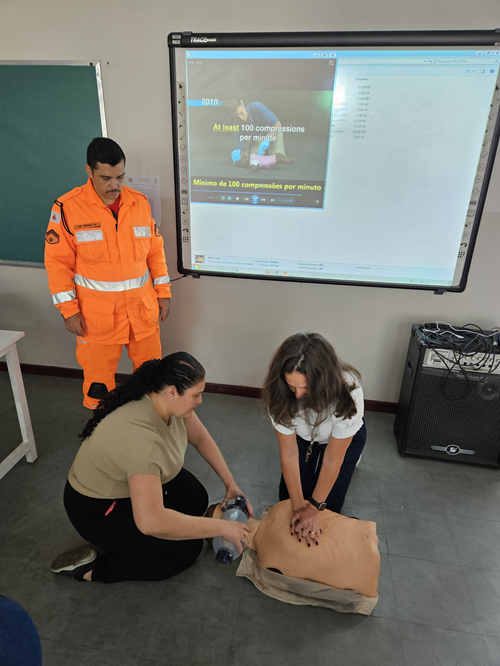 Treinamento de primeiros socorros: participantes praticam RCP com boneco sob orientação de instrutor do Corpo de Bombeiros em sala de aula.