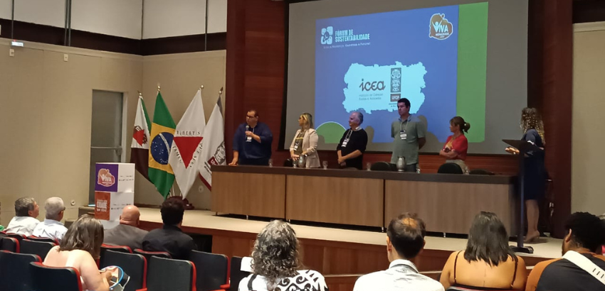 A imagem mostra uma bancada composta por seis pessoas. Ao fundo há um banner com o nome do Instituto de Ciências Exatas e Aplicadas