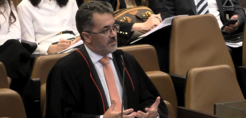 Foto de homem branco sentado, olhando para a direita e gesticulando enquanto se pronuncia na audiência do Tribunal Judicial de Minas Gerais