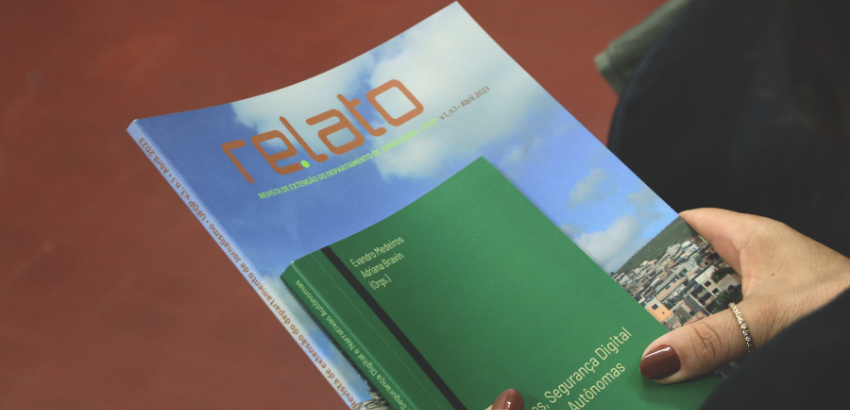 Imagem de uma mão segurando a revista azul Re.lato e o  livro verde Ativismos, Segurança Digital e Narrativas Autônomas