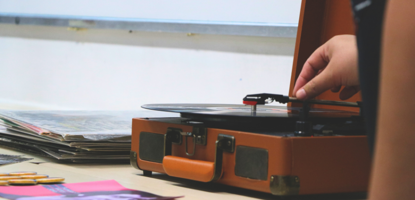 Uma mão abaixando a agulha de uma vitrola para tocar um disco LP