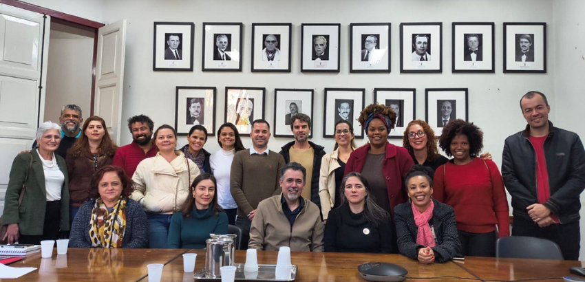 Foto coletiva do encontro entre integrantes da Reitoria da UFOP e do Coletivo Andorinhas. Aproximadamente 22 pessoas estão reunidas em uma sala institucional, todos sorriem para a camêra.