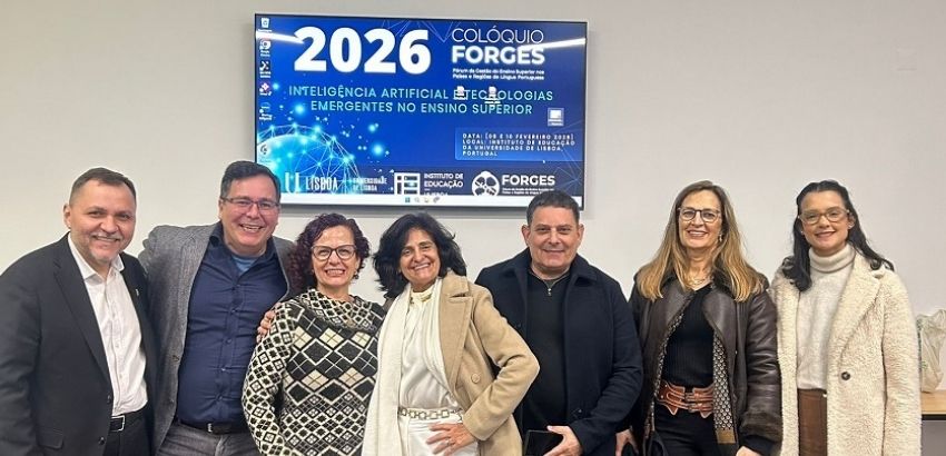 Sete pessoas posam juntas em um ambiente interno, sorrindo para a câmera, com um painel ao fundo anunciando o “Colóquio FORGES 2026” sobre inteligência artificial no ensino superior.