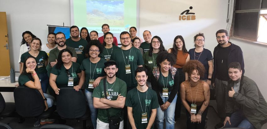 Grupo de participantes posa para foto em sala do ICEB, na UFOP, durante atividades da Caravana da Diversidade. Pessoas sorriem em pé e sentadas, com crachás de identificação e camisetas verdes.