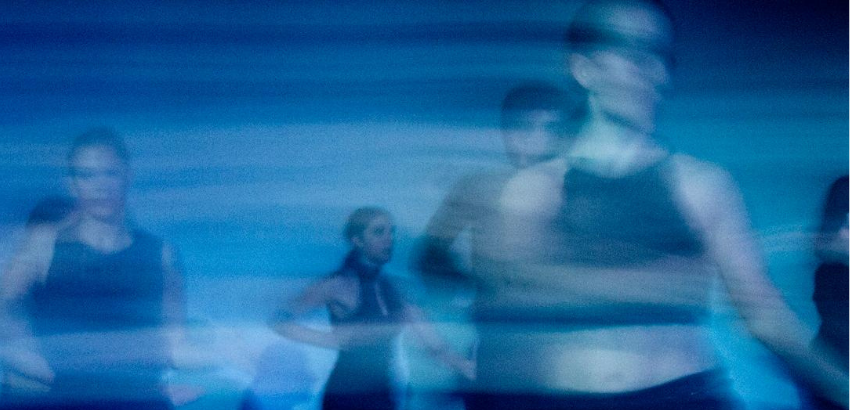 Foto de pessoas desfocadas dançando, com fundo azul-claro e escuro para trazer o contraste 