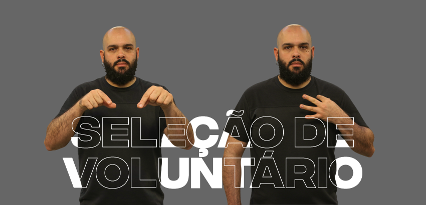 Homem com barba e camiseta preta fazendo sinais em Libras, com o texto 'SELEÇÃO DE VOLUNTÁRIO' em destaque sobreposto à imagem. Fundo cinza.