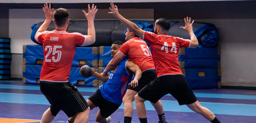 Jogador de handbol com a bola em mão, cercado pelo time adversário