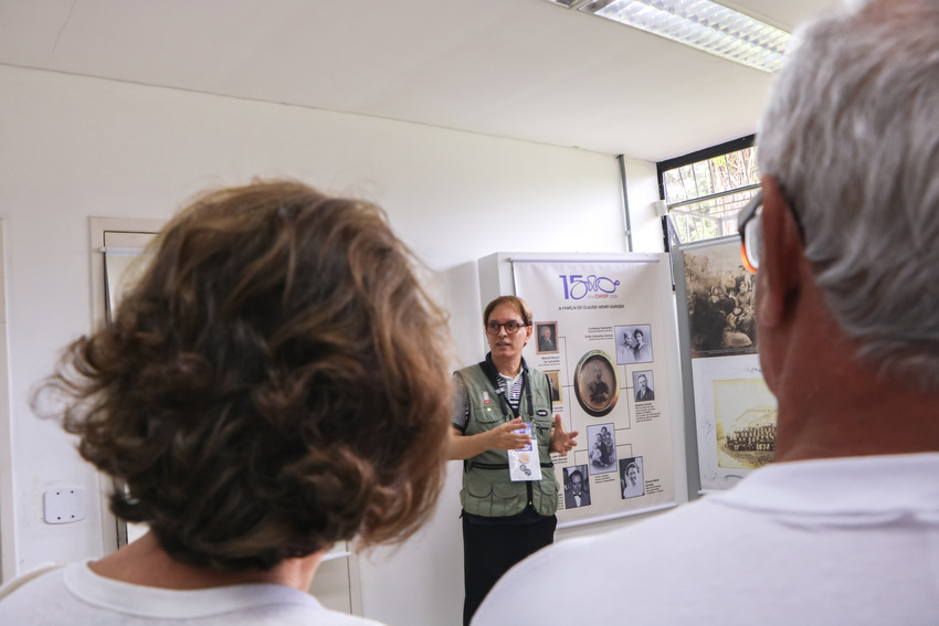 Apresentação sobre a história da EMOP 2026 durante visita à exposição comemorativa dos 150 anos da instituição.