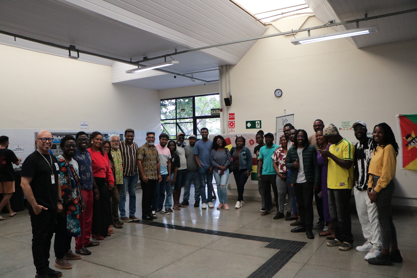 Grupo de estudantes, professores e servidores reunidos no Restaurante Universitário da UFOP durante a celebração do Dia da África. Os participantes posam em semicírculo dentro do espaço do RU, decorado com bandeiras africanas ao fundo. A atividade integro
