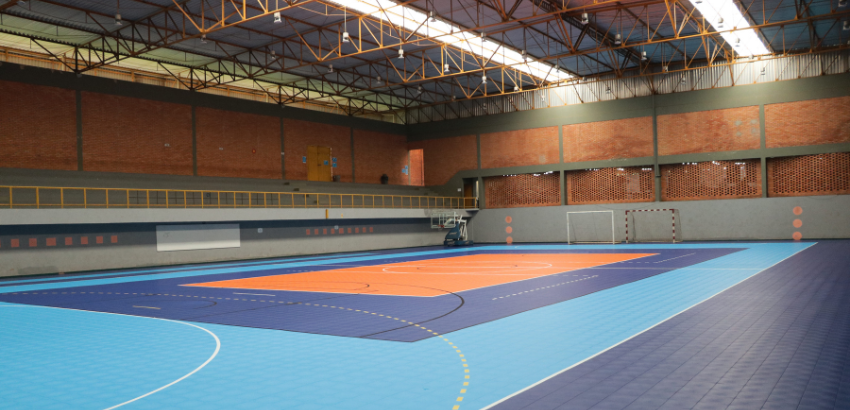 Imagem de uma quadra esportiva com piso nas cores azul claro e escuro e ao meio centralizado, um pequeno espaço em cor alaranjada