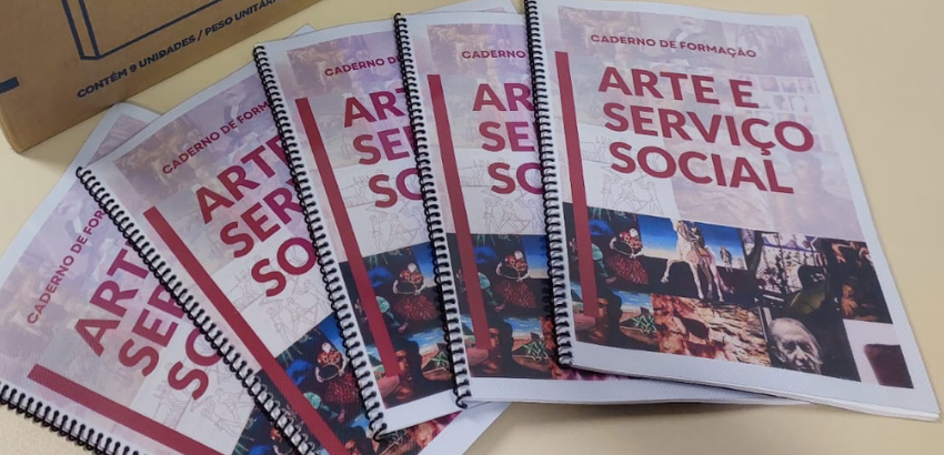 Cinco exemplares encadernados do “Caderno de Formação: Arte e Serviço Social” estão dispostos em leque sobre uma mesa clara. As capas trazem título em vermelho e uma faixa inferior com colagem de imagens artísticas e culturais.