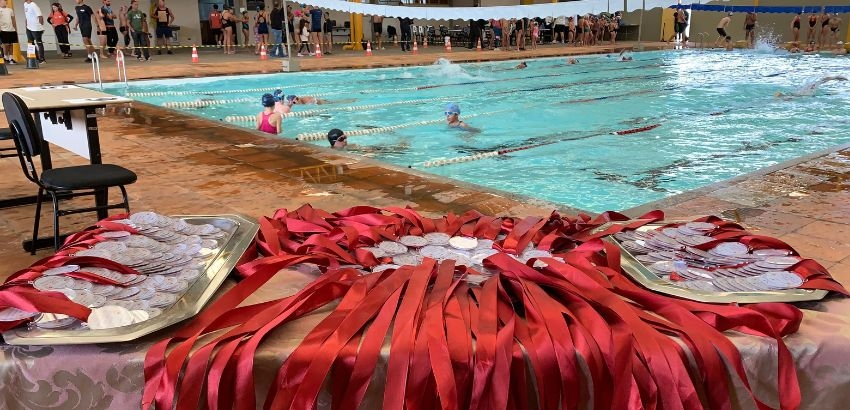 medalhas e a piscina de fundo com os atletas ao fundo