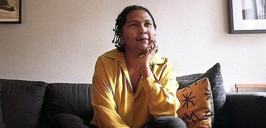 Foto de Bell Hooks, uma mulher negra, de aproximadamente 60 anos. Seus cabelos são tranças até os ombros e ela usa uma camisa de botão amarela.