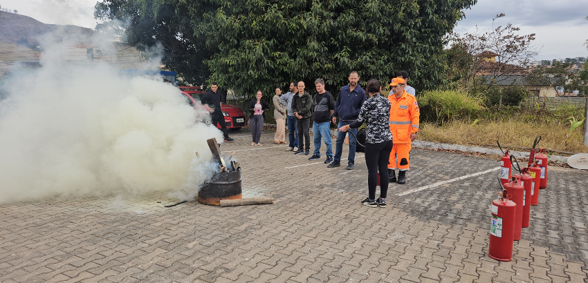 Treinamento de brigada com simulação de incêndio; participantes observam enquanto instrutores orientam o uso de extintores.