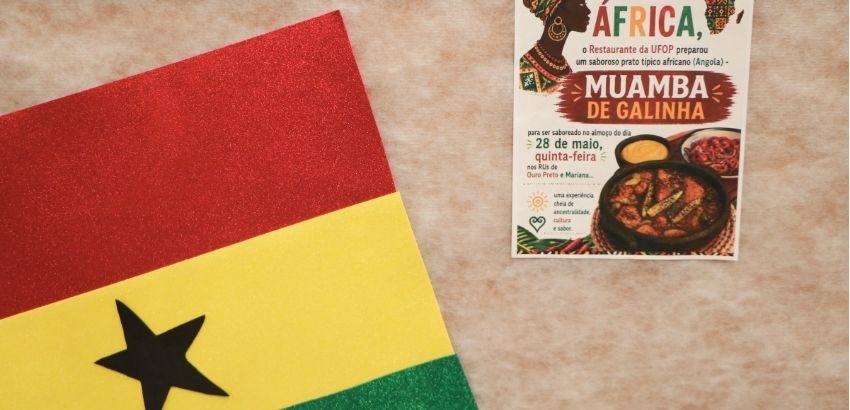 Banner de divulgação do prato “Muamba de Galinha”, preparado pelo Restaurante Universitário da UFOP em celebração ao Dia da África. Em primeiro plano, aparece parte da bandeira de Gana nas cores vermelho, amarelo e verde, com uma estrela preta ao centro.