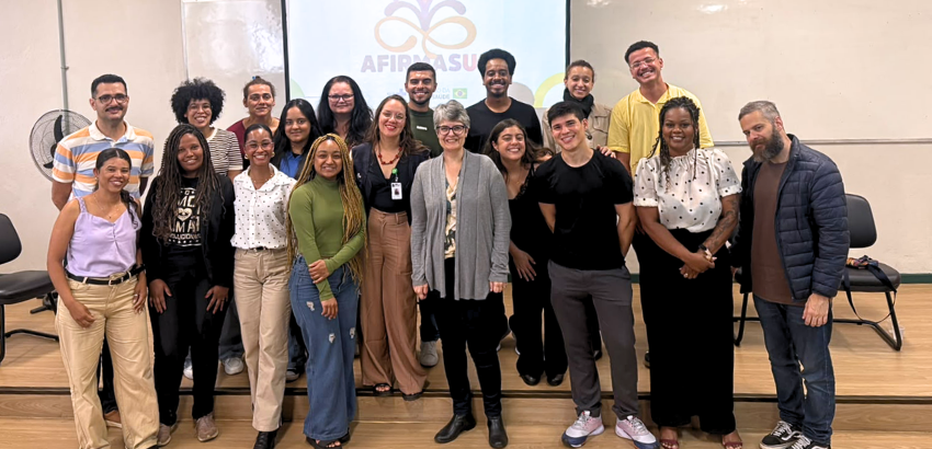 Grupo de pessoas posa para foto em um auditório, diante de uma tela com o logotipo da AfirmaSUS