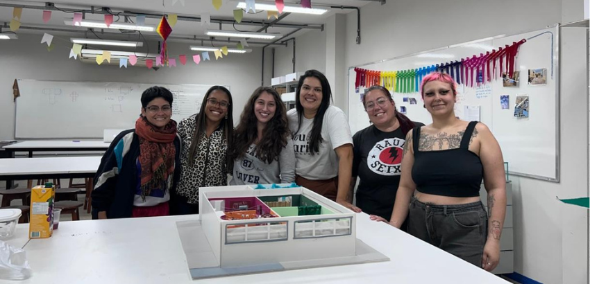 Parte da turma de Museologia reunida ao redor de uma maquete sobre uma mesa