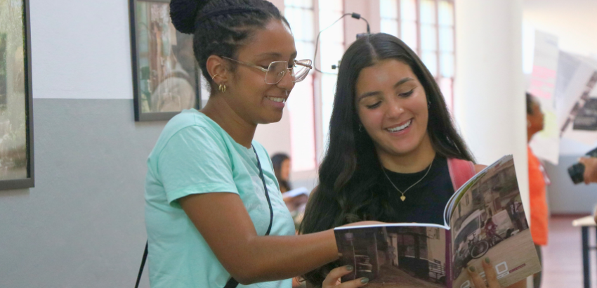 Duas meninas encaram a revista re.latos aberta aberta em suas mãos.