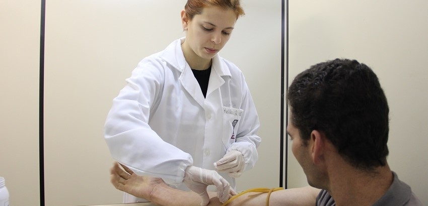 Profissional de saúde em pé tirando sangue de um homem no laboratório