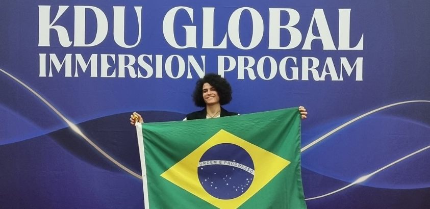 Iago, sorridente e ao centro, segura uma bandeira do Brasil.