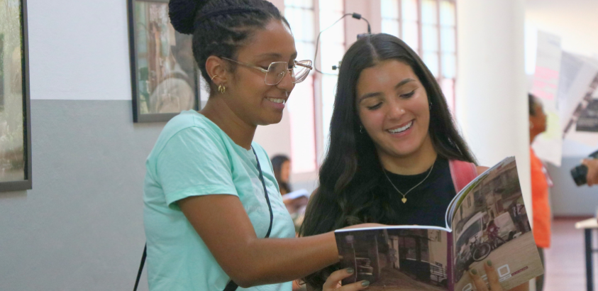 Duas meninas encaram a revista re.latos aberta aberta em suas mãos.