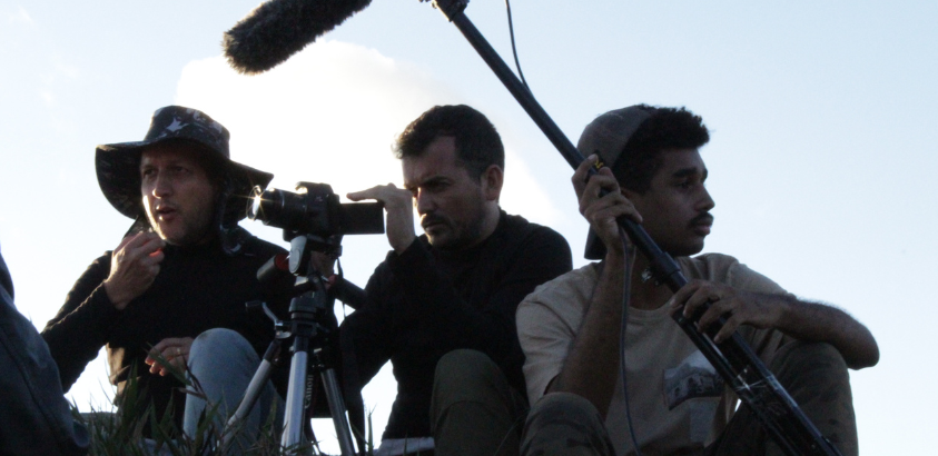 Equipe do audiovisual da UFOP sentada em um campo com seus equipamentos.